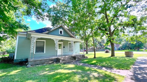 the front of a blue house with trees and a sidewalk