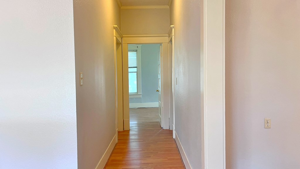 a hallway with wood floors and white walls and a window