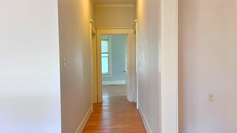 a hallway with wood floors and white walls and a window