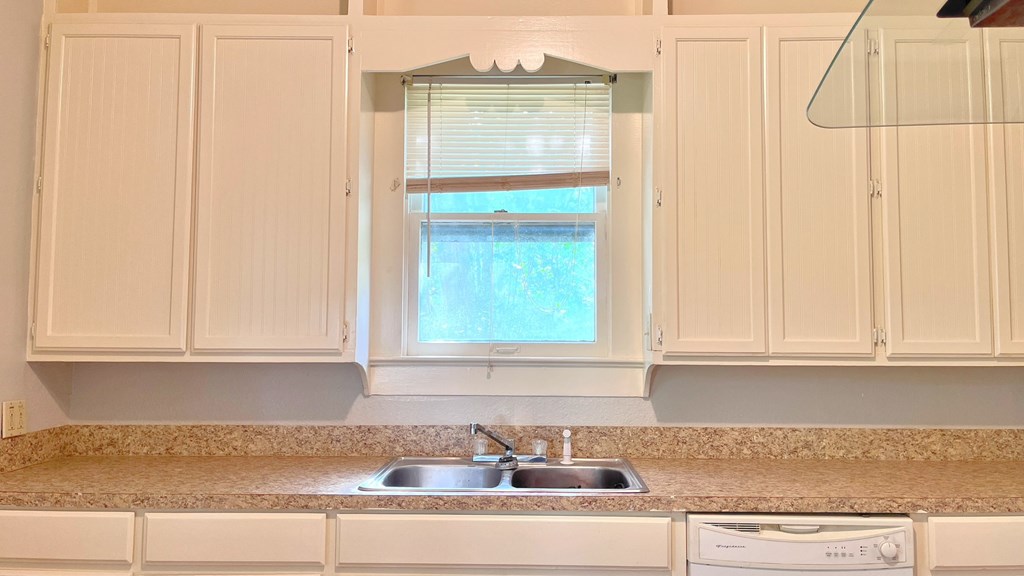 a kitchen with white cabinets and a window above a sink