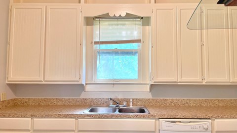 a kitchen with white cabinets and a window above a sink