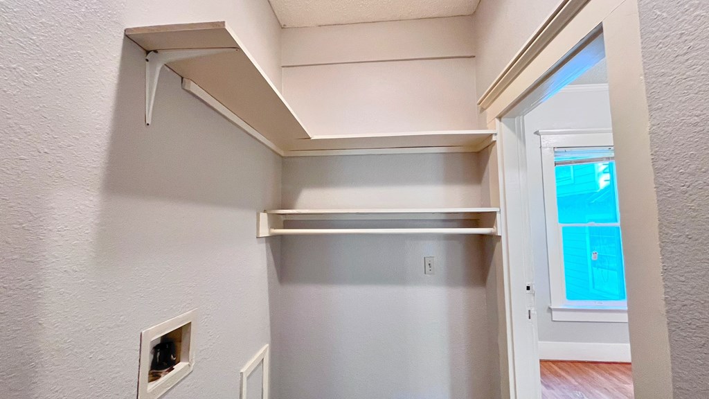 a walk in closet in a home with white walls and a window
