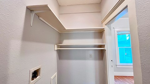 a walk in closet in a home with white walls and a window