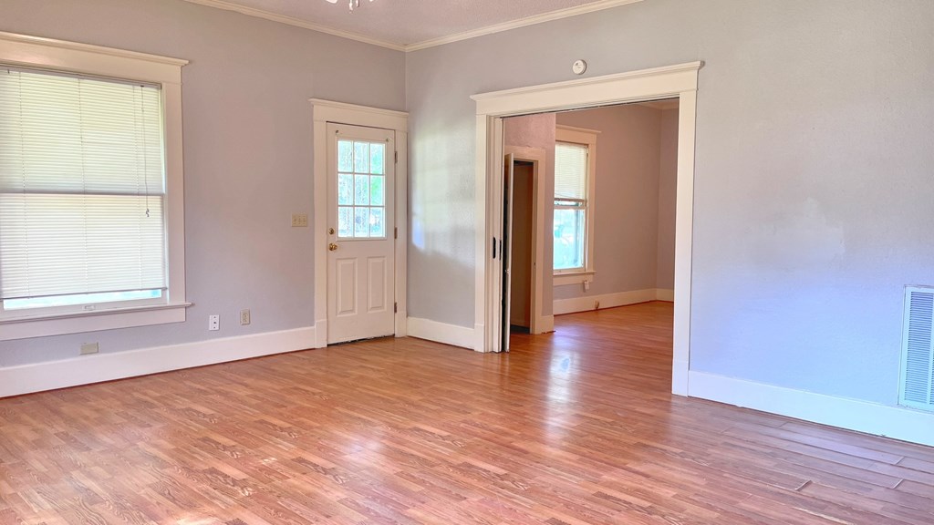 an empty living room with a hard wood floor and a door to a bedroom