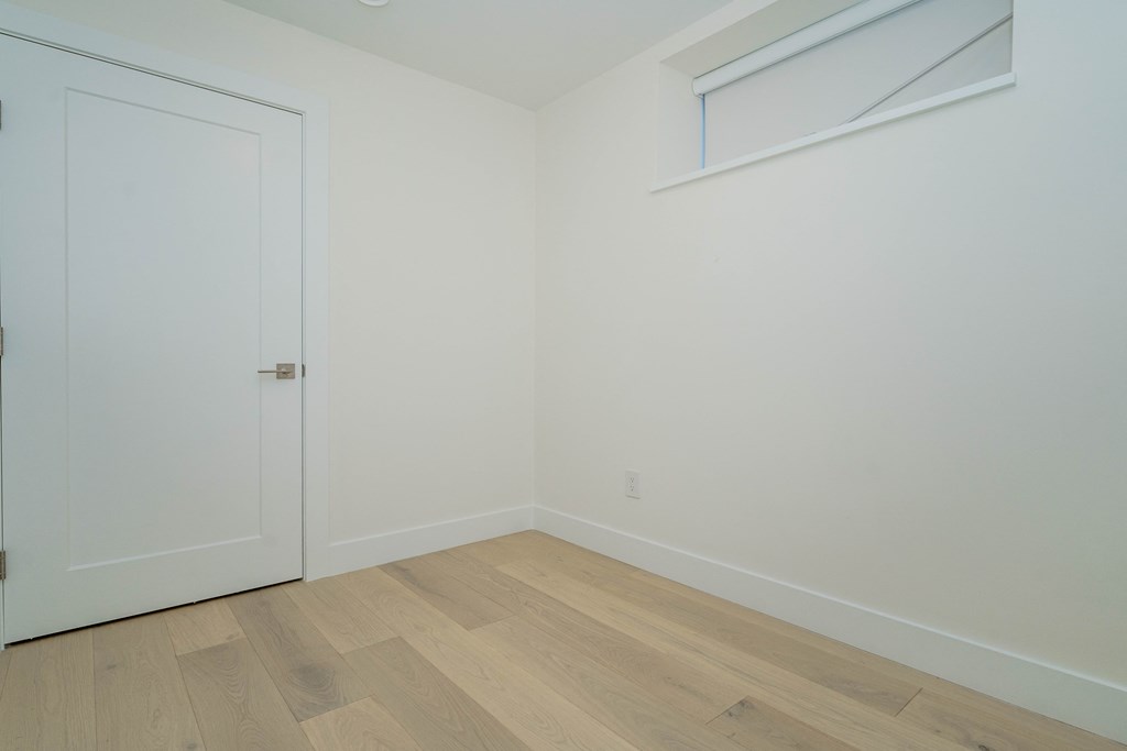 a bedroom with white walls and wood flooring and a window