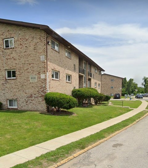 A brick apartment building with green bushes in front.