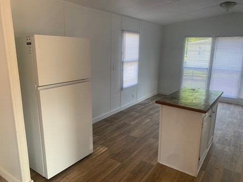 A white refrigerator is in a kitchen with wood floors and white cabinets.