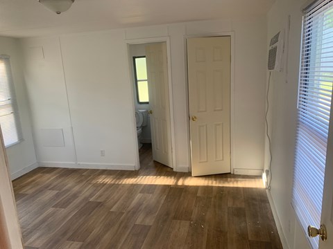 A room with wooden floors and white walls, with a door on the right and a window on the left.