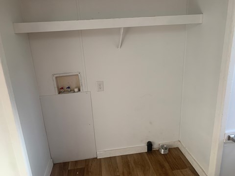 A white wall with a small shelf and a black object on the floor.