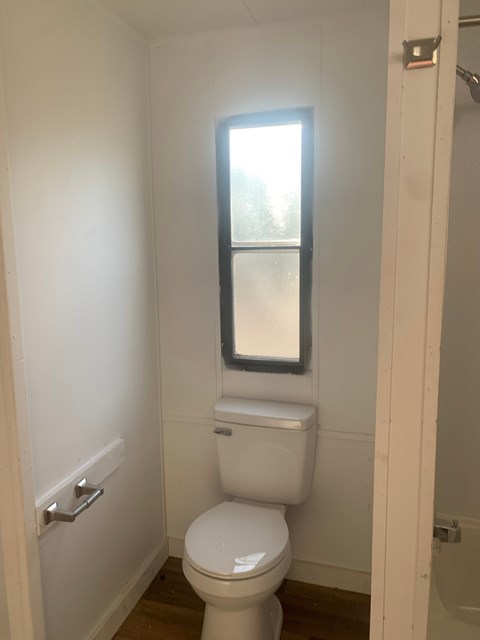 A white toilet in a small bathroom with a window above it.