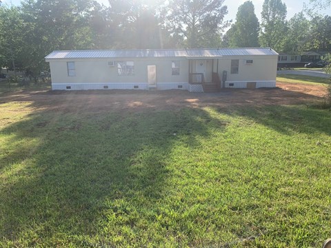 A white house with a metal roof is surrounded by a grassy area.
