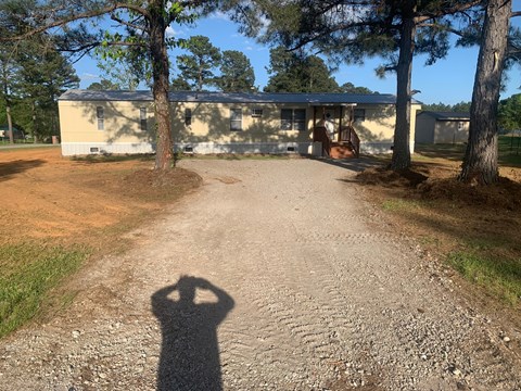 A shadow of a person is cast on a gravel path leading to a building.