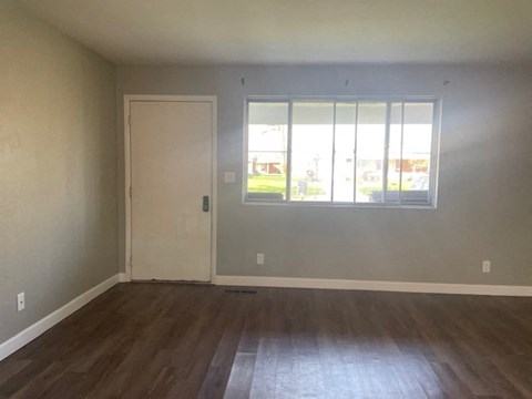 an empty living room with a window and wooden floors