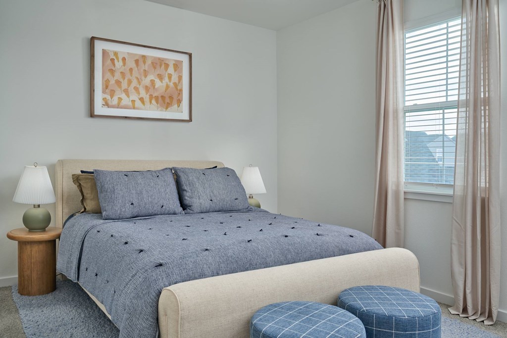 A bed with a blue comforter and matching ottoman with a lamp on a side table.