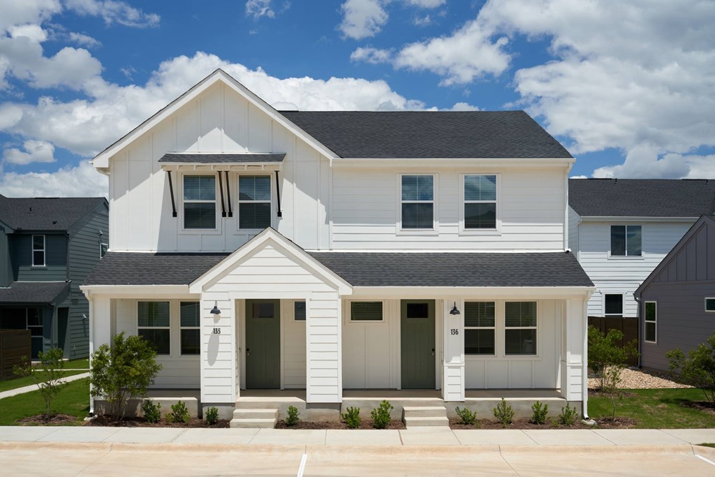 A white two-story house with a black roof and a grey garage door.