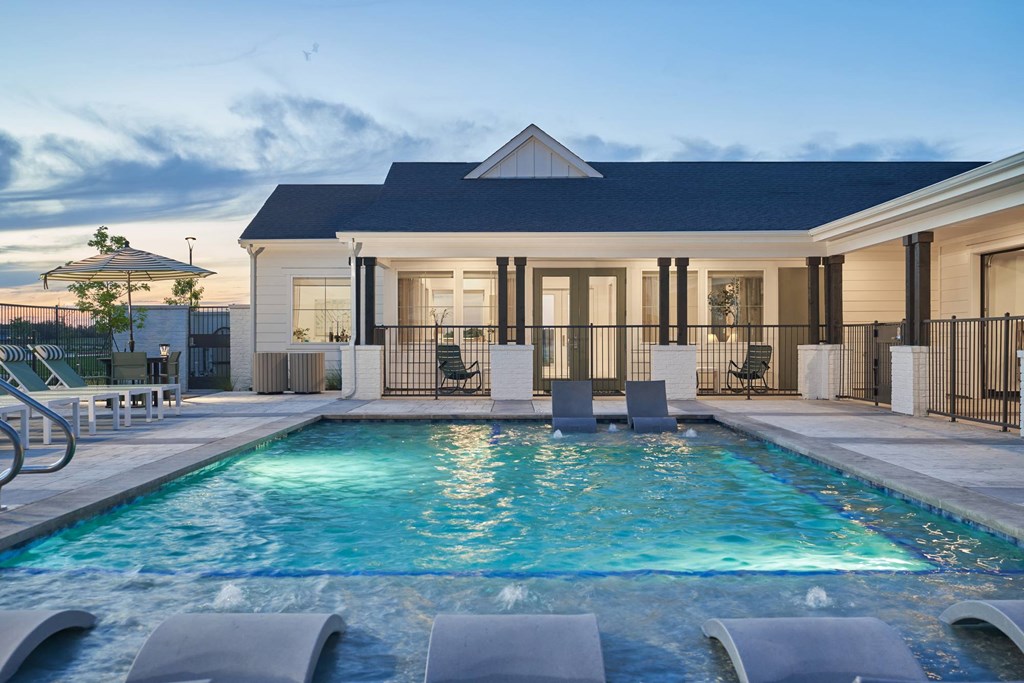 A pool in front of a house with a black fence.