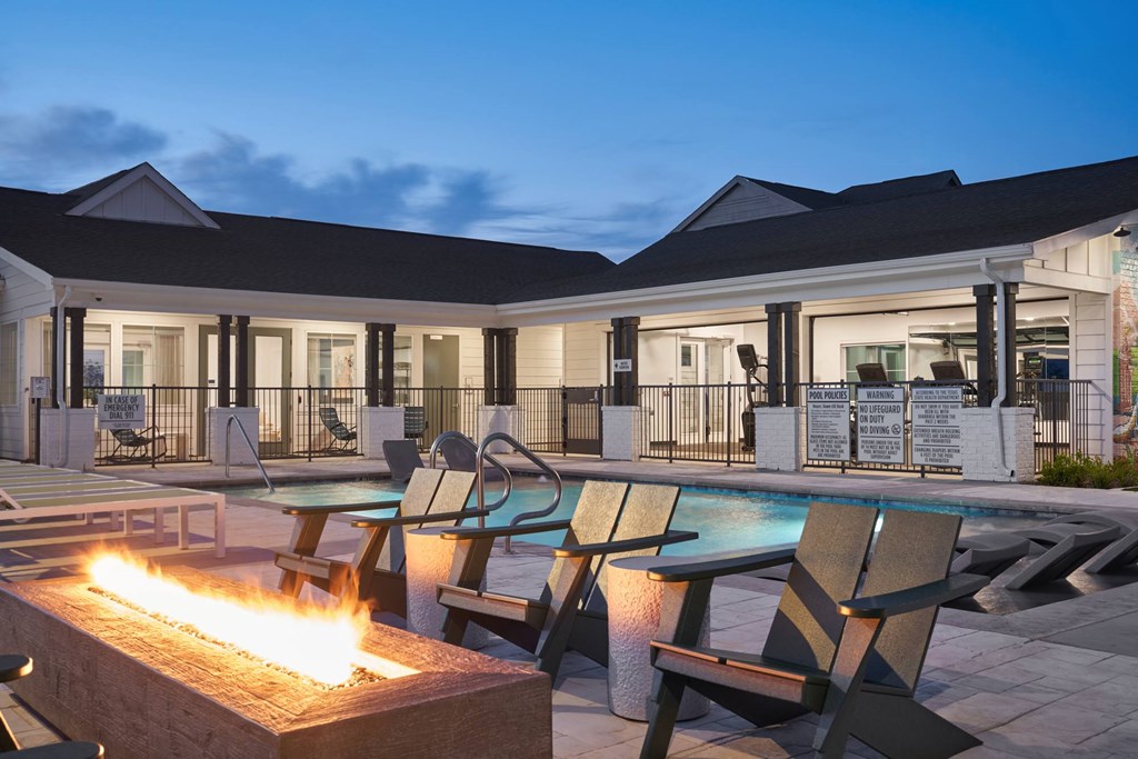 A poolside area with a fire pit in the foreground and lounge chairs around the pool.