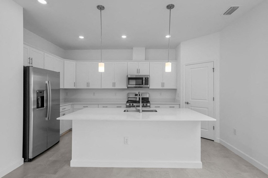 a white kitchen with a large island and a stainless steel refrigerator