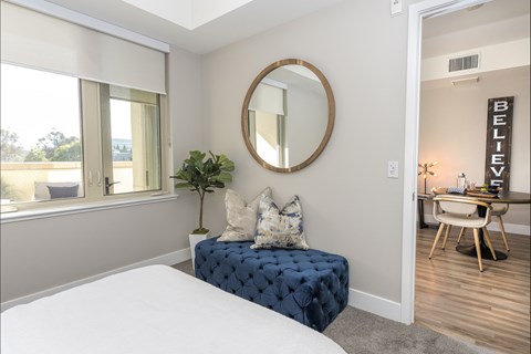 A bedroom with a round mirror and a blue bench.