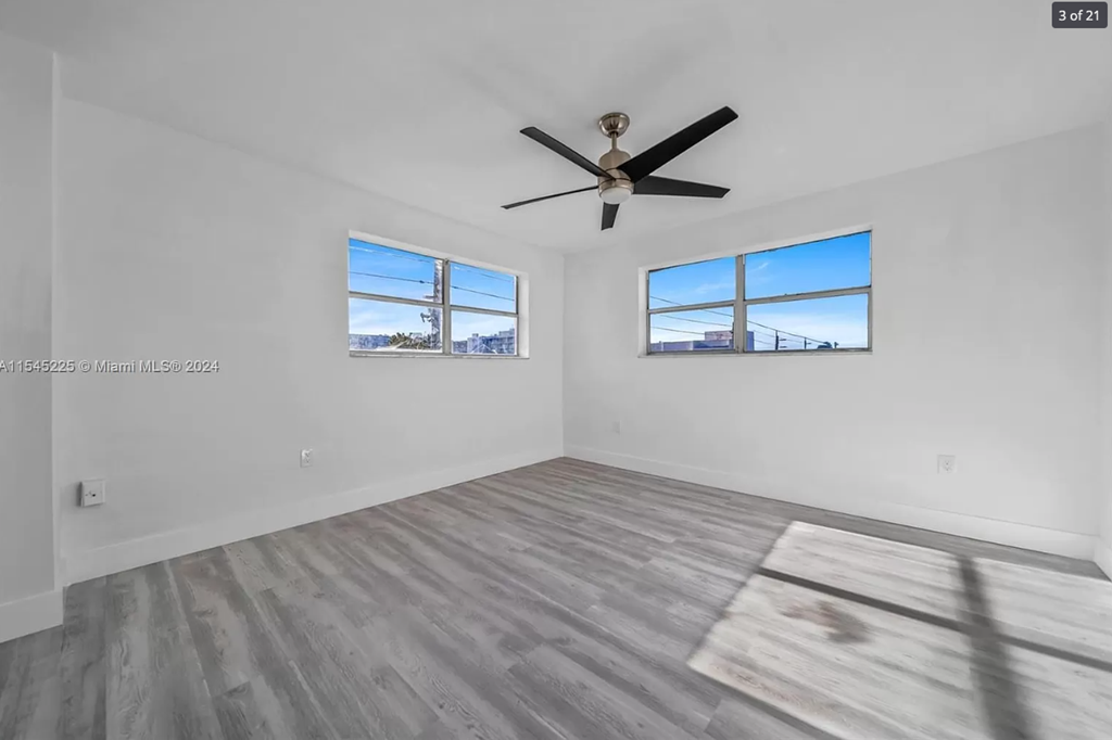 A room with a ceiling fan and two windows.