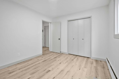 A room with white walls and wooden flooring, featuring a door and a wardrobe.