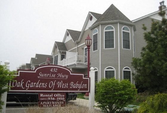 a sign for the oak gardens of west babylon in front of a house