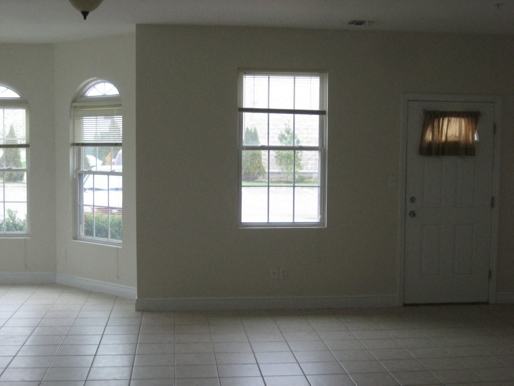 an empty living room with a door and three windows