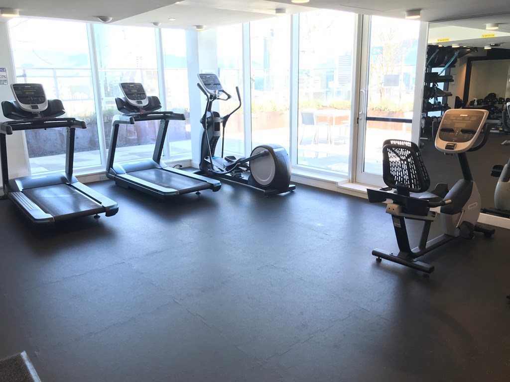 a workout room with treadmills and other exercise equipment in a building with windows