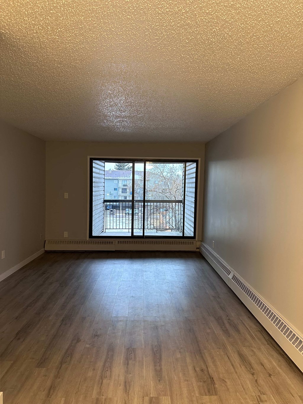 an empty living room with wood floors and a large window