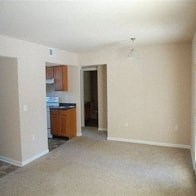 an empty living room with a kitchen in the background