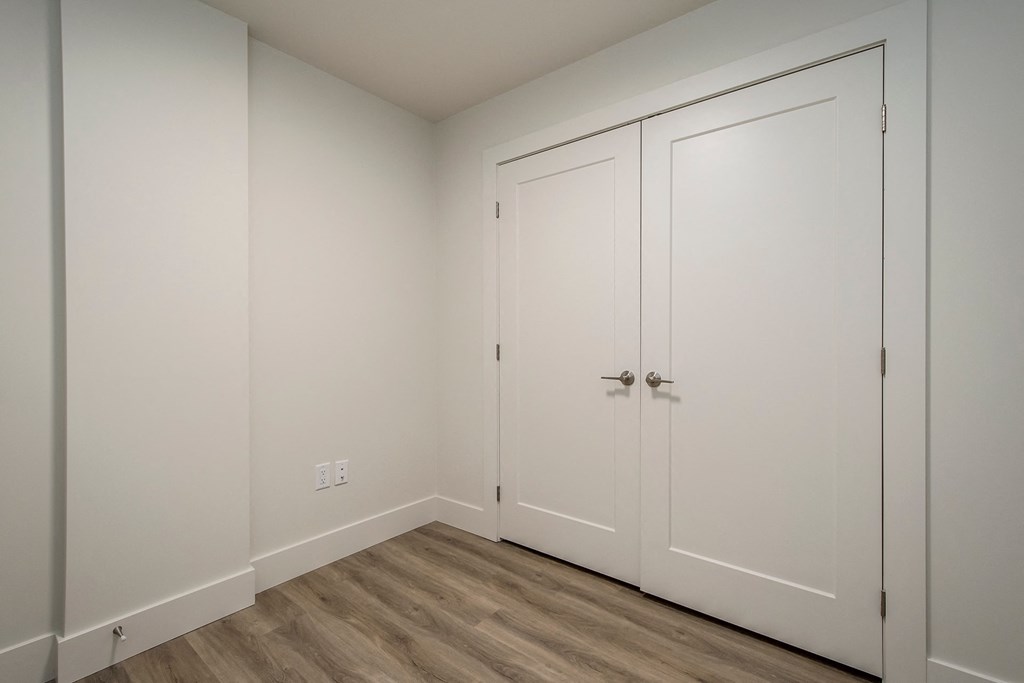 a bedroom with white walls and white closets and wood floors