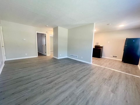 an empty living room with wood flooring and a black refrigerator