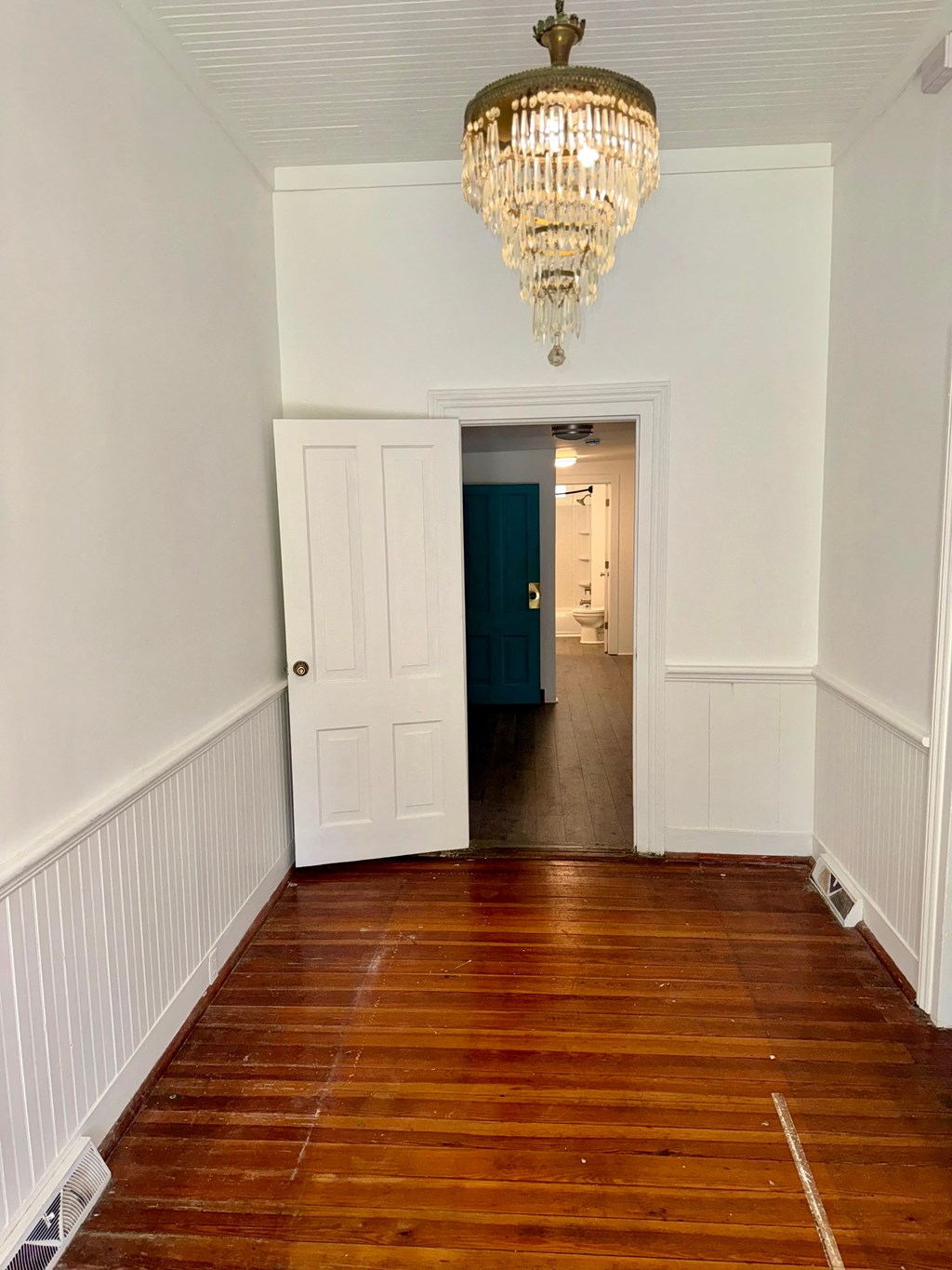 a hallway with white walls and a wooden floor and a chandelier