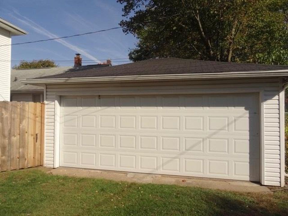 A white garage door is closed and has a wooden fence on the left side.