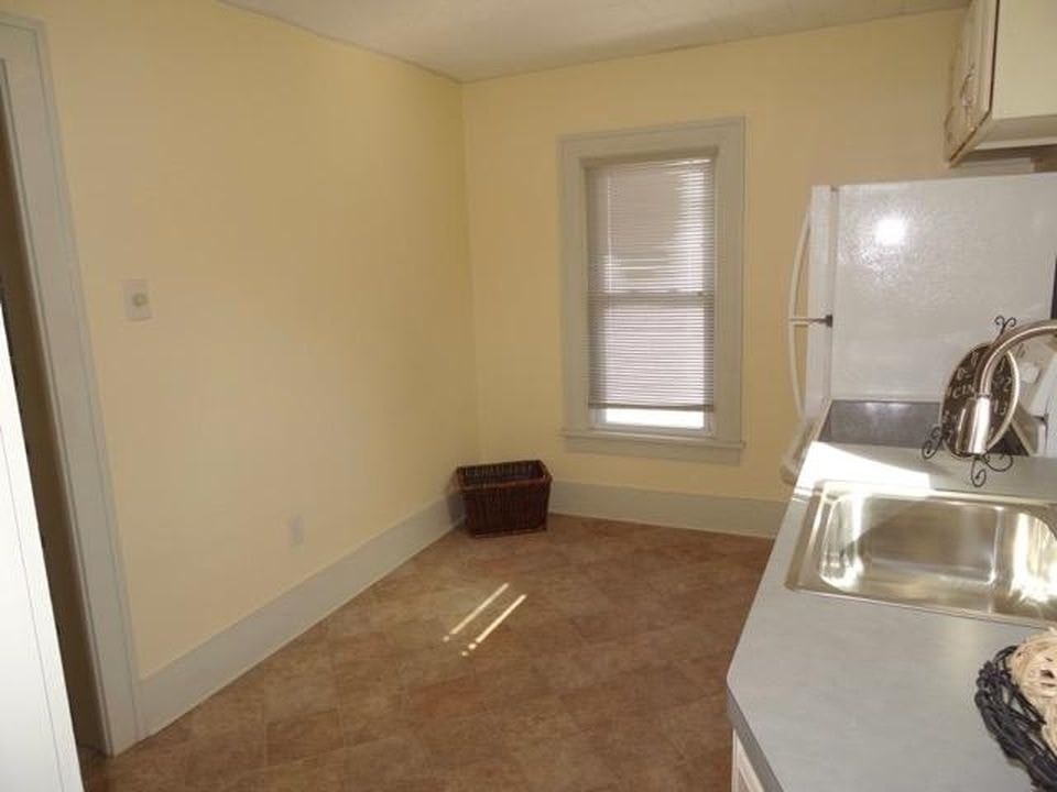 A kitchen with a white fridge, sink, and a window with blinds.