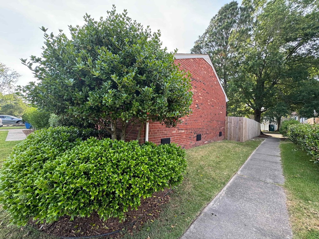 the side of a brick building with a tree and a sidewalk