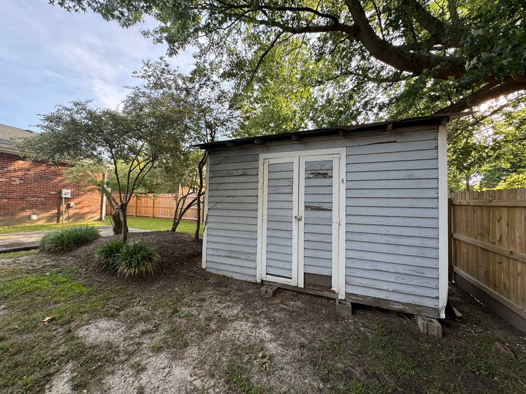 a small white shed with white shutters on the side of a yard