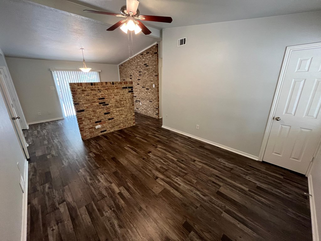 an empty living room with wood flooring and a brick wall
