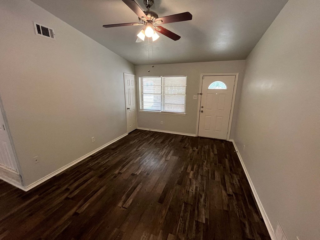 an empty living room with hardwood floors and a ceiling fan