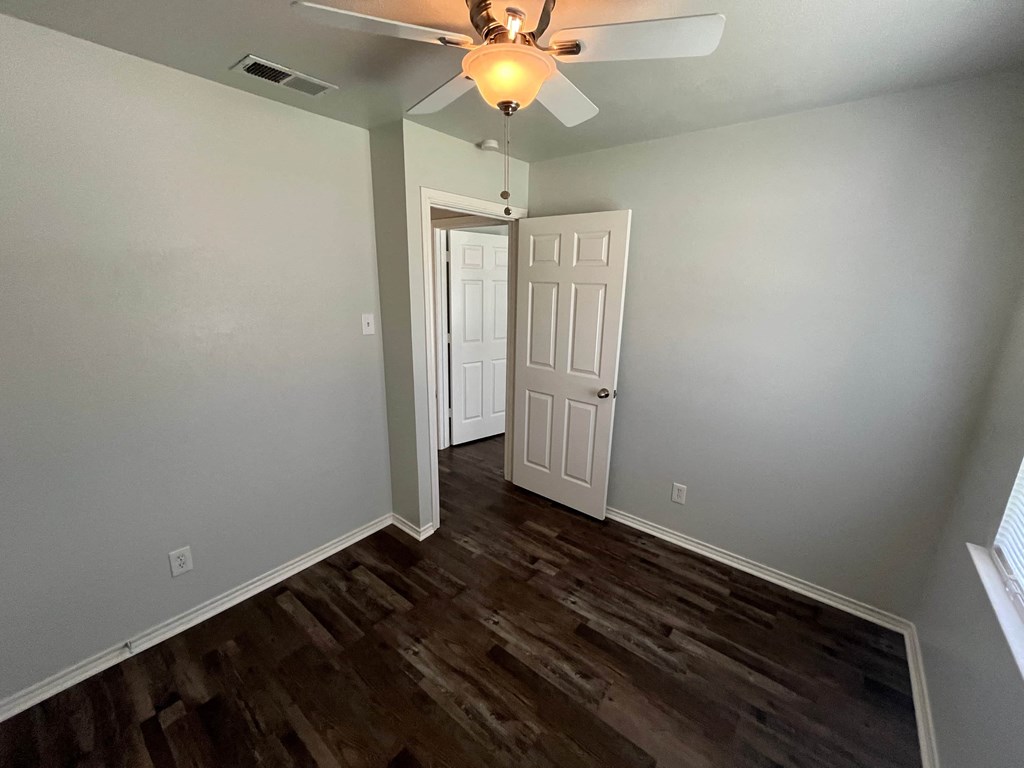 an empty living room with wood floors and a ceiling fan