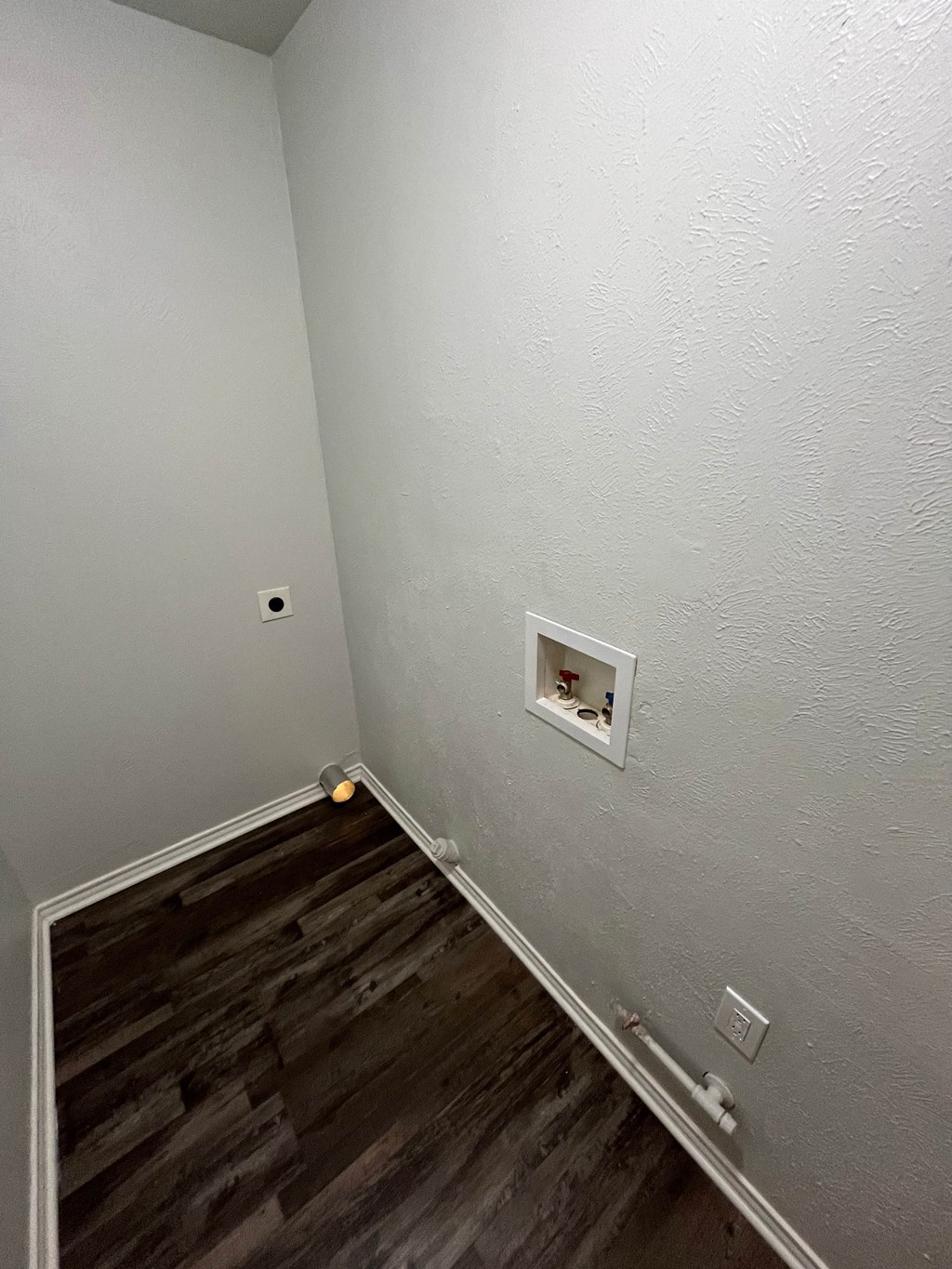 a small room with a wooden floor and a white outlet on the wall