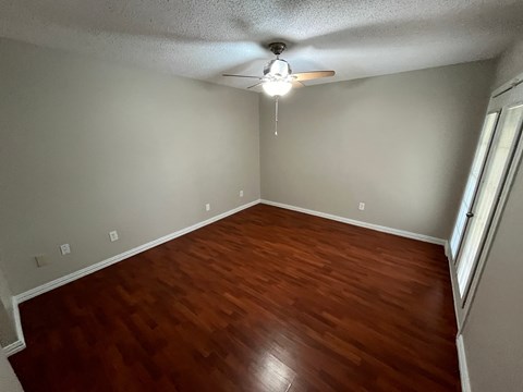 an empty living room with wood floors and a ceiling fan
