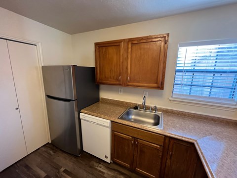 A kitchen with a black fridge, white dishwasher and wooden cabinets.