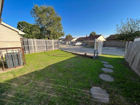 A backyard with a fence, a pathway, and a grassy area.