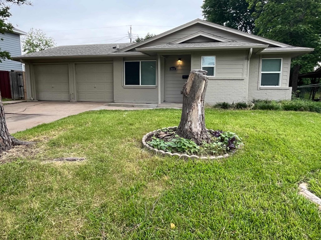 A house with a grey roof and a tree stump in the front yard.