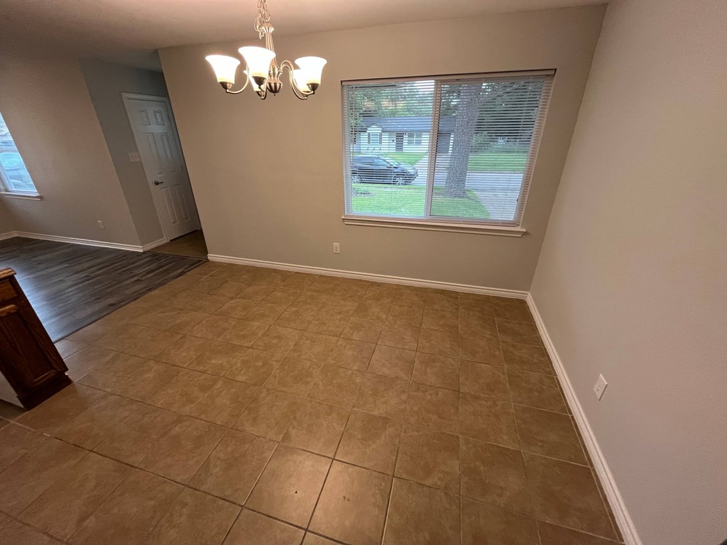 A room with a brown tile floor and a window showing a tree and a car outside.