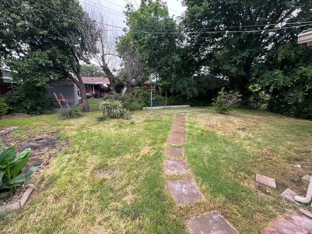 A backyard with a grassy area, a stone path, and a tree.