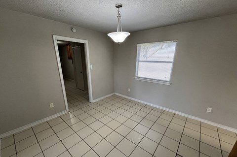 an empty living room with tiled floors and a door to a hallway