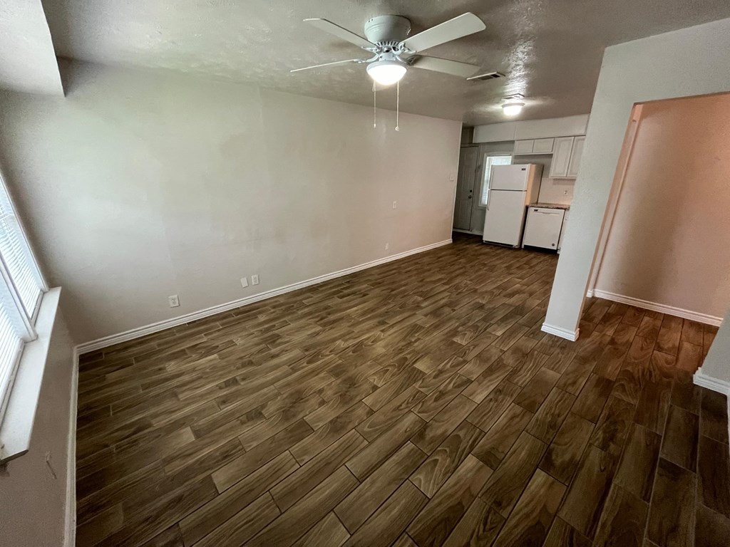 an empty living room with wood flooring and a ceiling fan