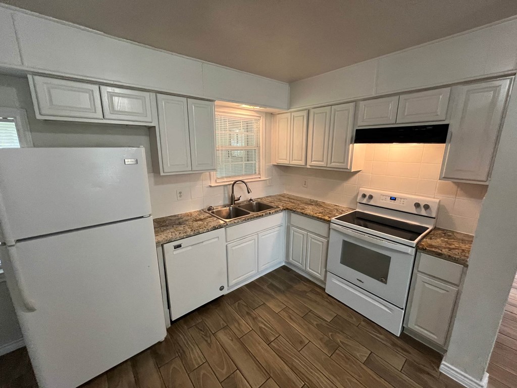 a kitchen with white cabinets and white appliances and wood flooring